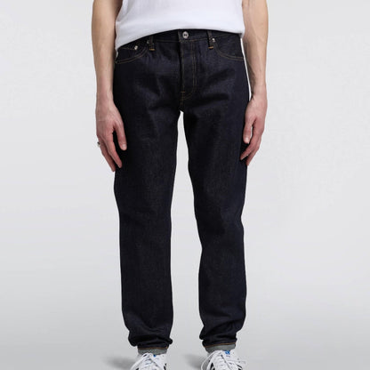 Person wearing dark jeans and white sneakers on a plain background