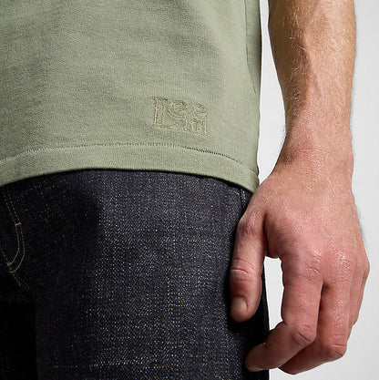 Person wearing a green t-shirt with a logo on a plain background