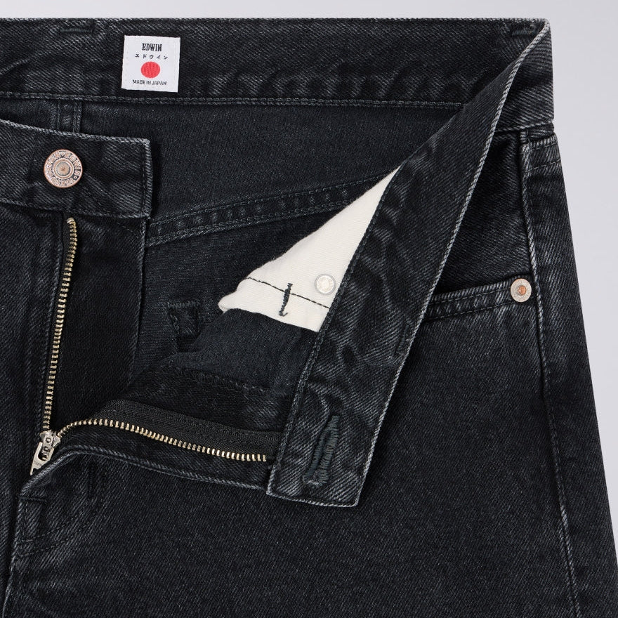 Close-up of black denim jeans with a brand label on a light gray background
