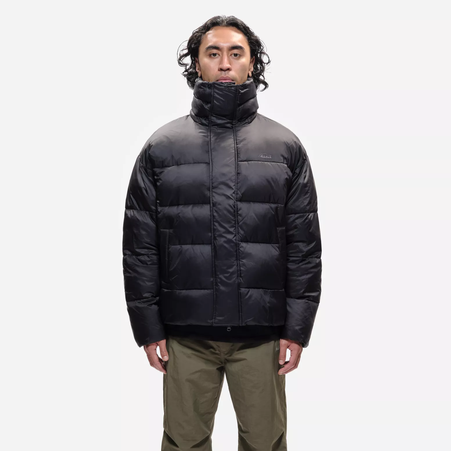 Person wearing a black puffer jacket and green pants on a white background