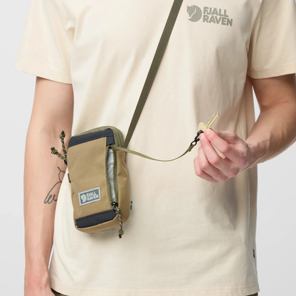 Person wearing a beige t-shirt with Fjäll Räven logo, holding a matching crossbody bag.