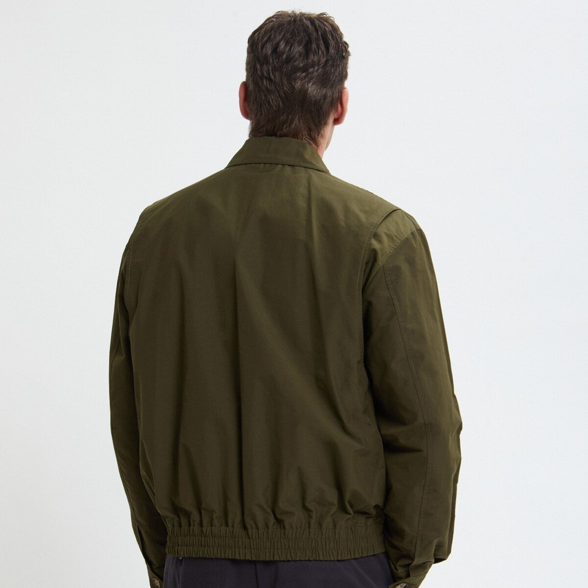 Person wearing a green jacket and dark pants on a white background