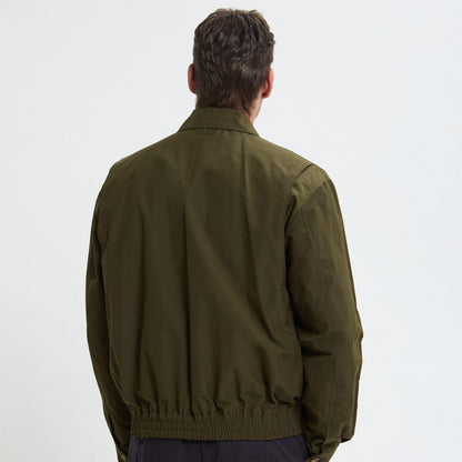 Person wearing a green jacket and dark pants on a white background