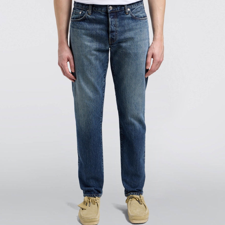 Person wearing blue jeans and beige shoes on a white background