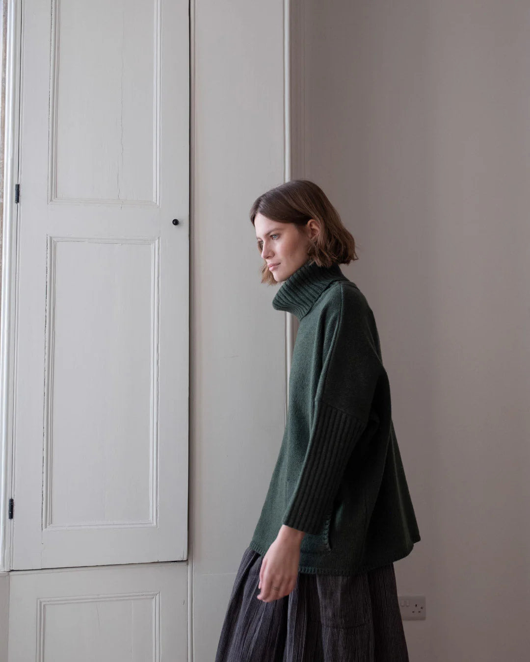 Woman wearing a green sweater standing in a room with neutral walls.