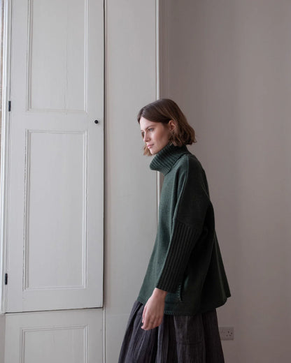 Woman wearing a green sweater standing in a room with neutral walls.