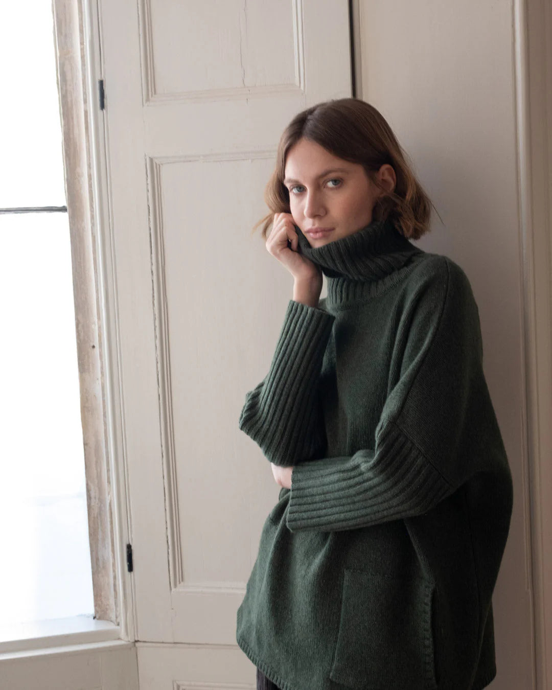 Woman wearing a dark green sweater - rollneck and long sleaves - 100% lambs wool sold at Regent Tailoring Salisbury 