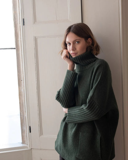 Woman wearing a dark green sweater - rollneck and long sleaves - 100% lambs wool sold at Regent Tailoring Salisbury 