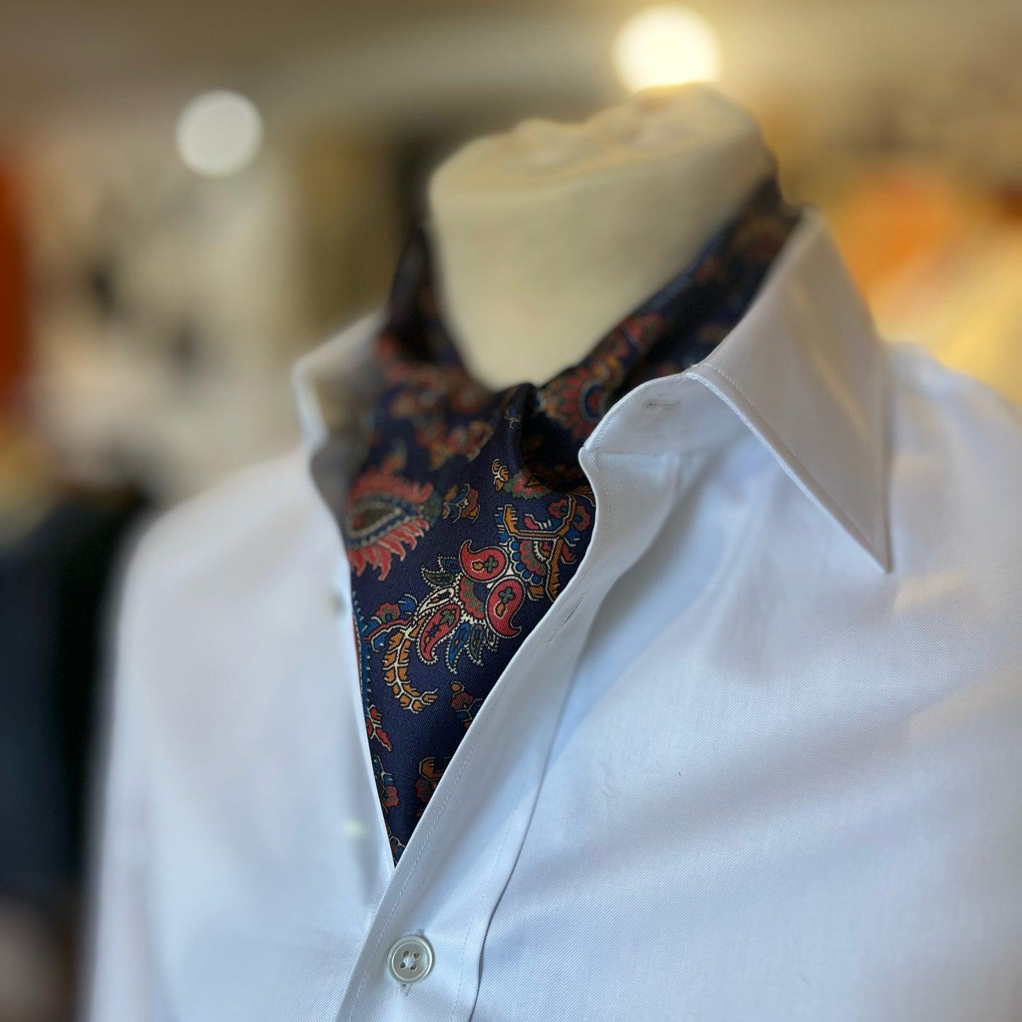 A blue tootal scarf with paisley pattern tied in a cravat style around the neck of a mannequin