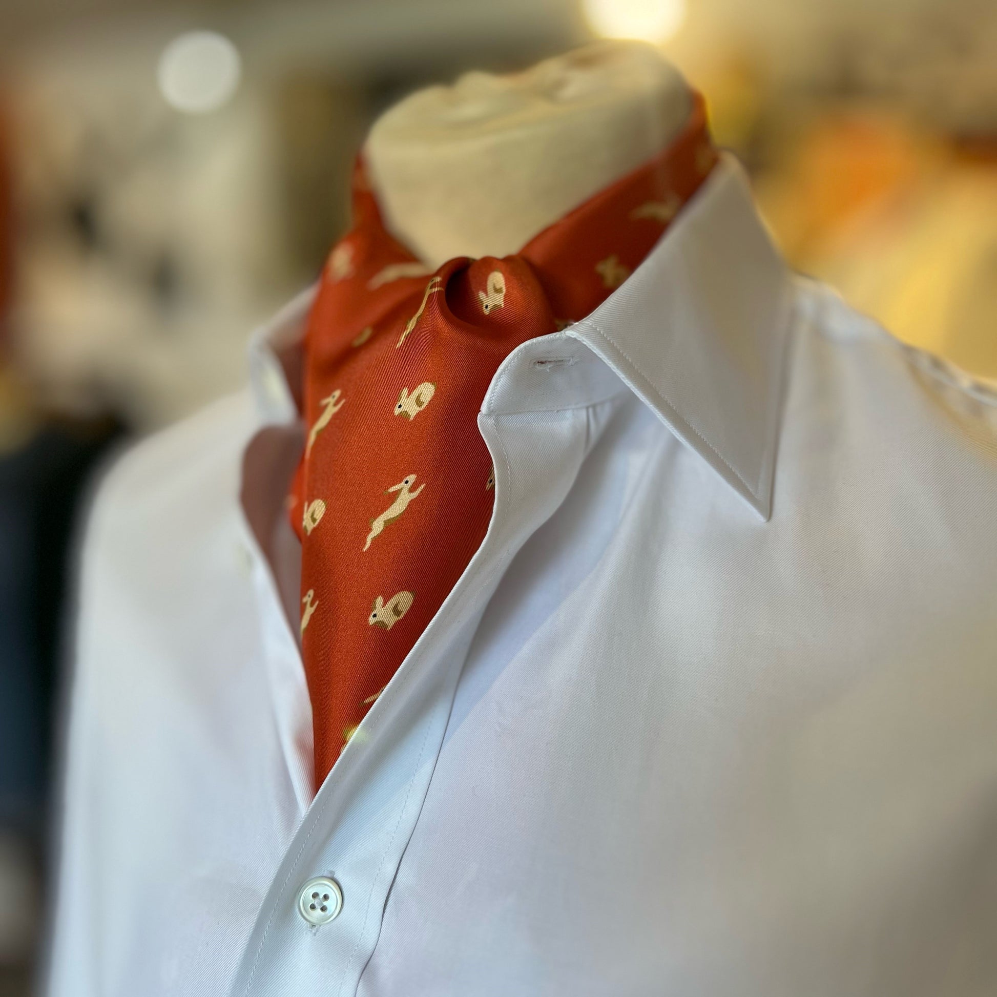 An orange tootal scarf with a printed pattern of bunny rabbits tied in a cravat style around the neck of a mannequin