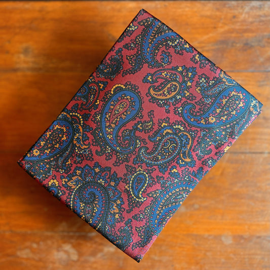 A folded red paisley tootal scarf with blue accents on a wooden background