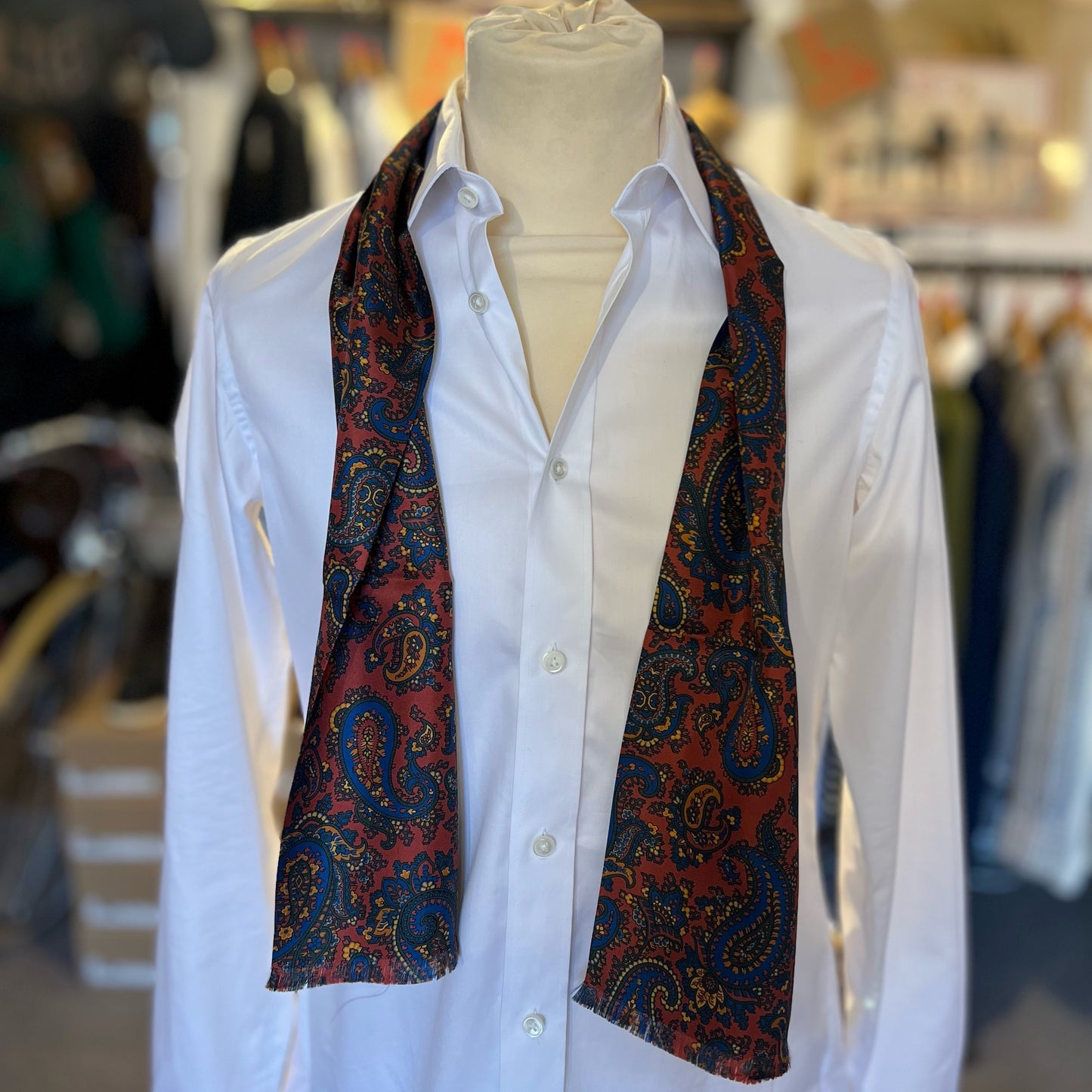 A red tootal scarf with a paisley pattern draped loosely around the shoulders of a mannequin.